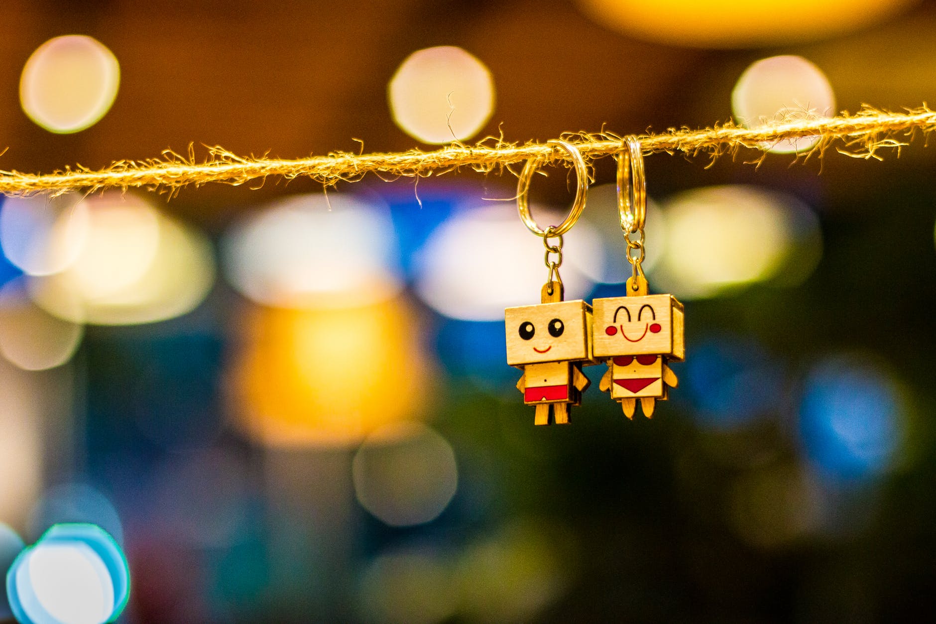 two man and woman wooden couple keychains hanging on rope overlooking bokeh lights